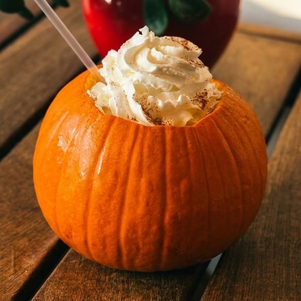 Pumpkin drink with whipped cream and cinnamon on a wooden table, with a red pot in the background.